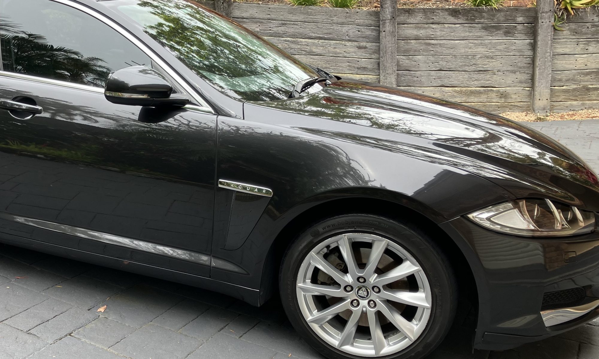 "Polished black Jaguar car on a driveway, showcasing a sleek and shiny exterior."